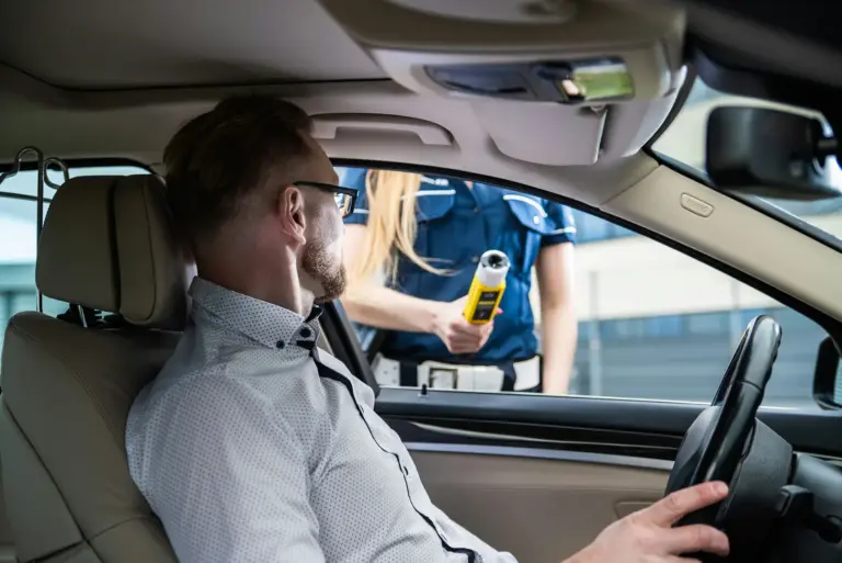 Kontrola drogowa kierowcy przez policję, test trzeźwości wykonywany alkomatem; zdjęcie ilustrujące sytuację prawną, w której pomoc doświadczonego adwokata i przygotowanie linii obrony mogą uchronić przed dożywotnim zakazem prowadzenia pojazdów.